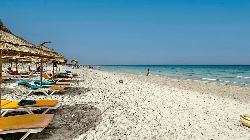 Peščena plaža s turkiznim morjem in slamnatimi senčniki